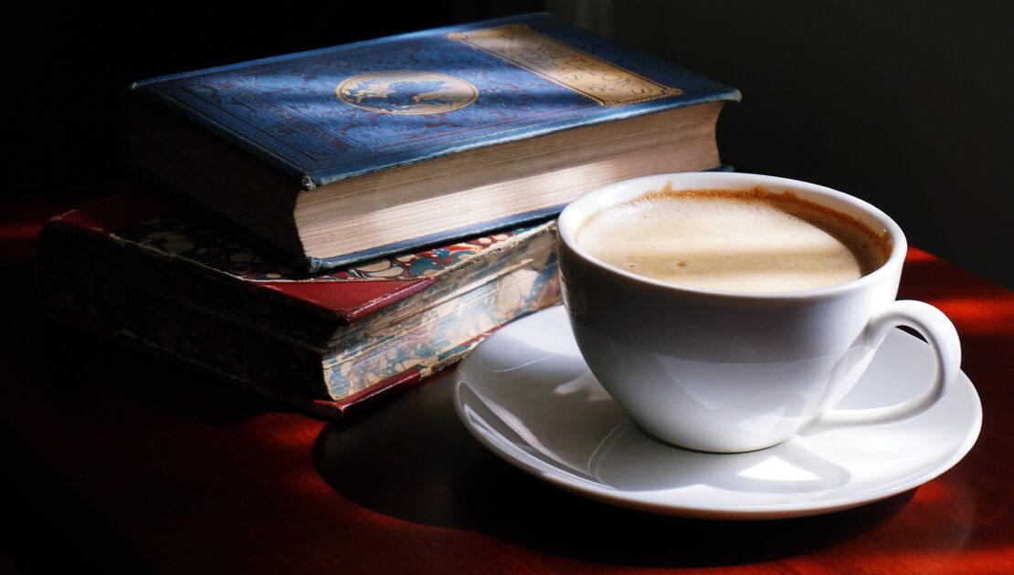Cup of coffee with 2 books on a table in a dark room.