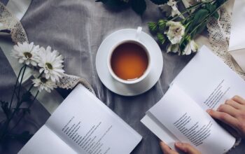 Image of someone reading books with a cup of coffee on a blanket.